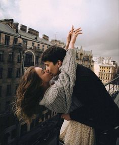 a man and woman kissing while standing on top of a building