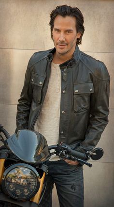 a man standing next to a motorcycle wearing a leather jacket and jeans with his hands in his pockets