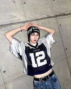 a young man wearing a football jersey holding his hands up to his head while standing in front of a concrete wall