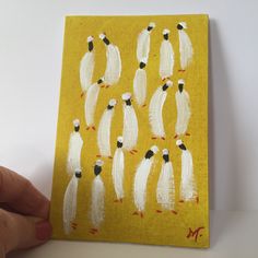 a hand is holding up a yellow painting with white birds on it