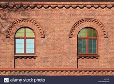 two arched windows on the side of a brick building with red bricks and green trim