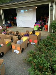 an image of people sitting in cardboard boxes on the ground with a projector screen behind them