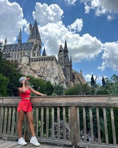 a woman in a red dress standing on a wooden deck near hogwarts castle