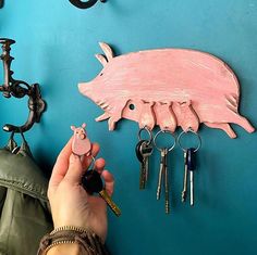 a person holding keys to a pig shaped key holder on a blue wall with hooks