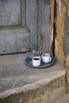 two cups of coffee are sitting on a plate next to a door with peeling paint