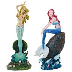 two mermaid figurines sitting on top of a rock next to each other,