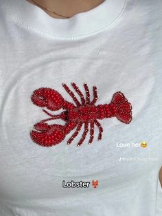 a woman wearing a white shirt with red lobster appliqued on it