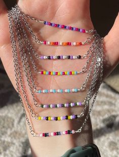 a person's hand holding a multicolored beaded chain bracelet and watch