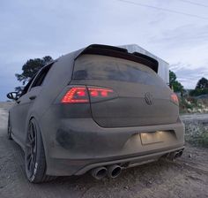 the rear end of a gray car parked on dirt