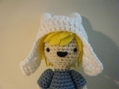 a crocheted doll wearing a white hat and blue dress with yellow hair sitting on top of a table