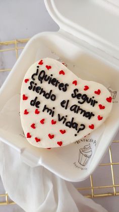 a heart shaped cake with writing on it sitting in a plastic container next to a white napkin