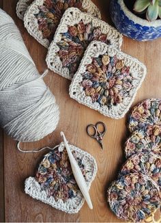 crocheted coasters, yarn and scissors on a wooden table with succulents