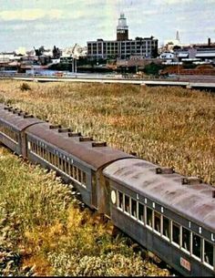 an old abandoned train traveling through the country side in front of a cityscape