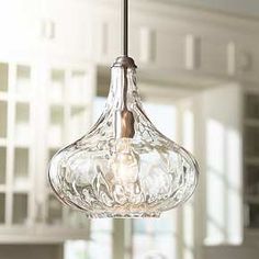 a clear glass light fixture hanging from a ceiling in a room with white cabinets and windows