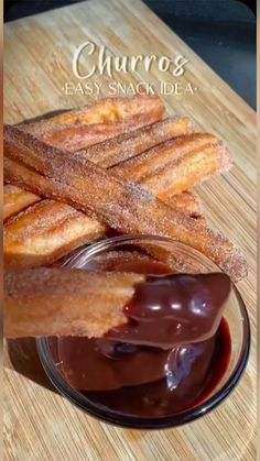 churros are being dipped with chocolate sauce on a wooden cutting board next to a bowl of dipping sauce