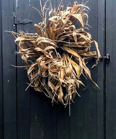 a wreath made out of dried corn on a black wooden door with metal latches