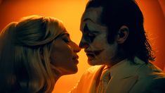 a man and woman dressed as the joker kiss in front of an orange background,