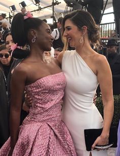 two women standing next to each other in front of a group of people on a red carpet