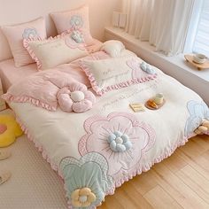 a bed with pink comforters and pillows on top of it in a room next to a window