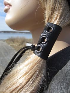 a mannequin head wearing a black leather choker with metal circles on it