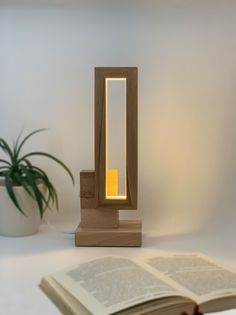 an open book sitting on top of a table next to a lamp and potted plant