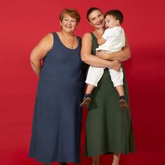 two women and a baby are posing for a photo in front of a red background