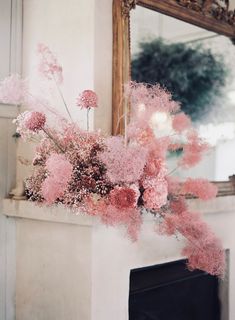 pink flowers sitting on top of a mantle in front of a mirror and fire place