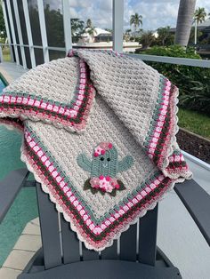 a crocheted blanket with a teddy bear on it sitting on a chair next to a pool