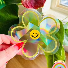a hand holding a flower shaped sticker with a smiley face on it