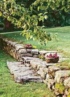 a stone wall in the middle of a grassy area with trees and bushes behind it