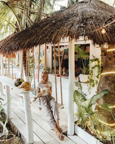 a woman sitting on a porch next to a palm tree holding a plate of food