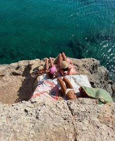 two people are laying on the rocks by the water with their backs to each other