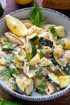 a bowl filled with pasta and vegetables on top of a wooden table next to lemons