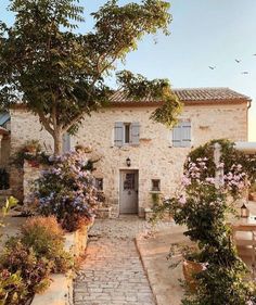 an old stone house with lots of flowers and trees