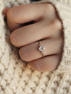 a woman's hand wearing a gold ring with a white diamond on the middle