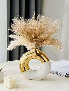 a white table with a gold and white vase filled with dry grass on top of it