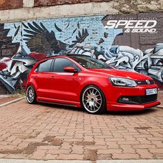 a red car parked in front of a graffiti covered wall