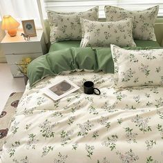 a bed with green and white sheets, pillows and a book on the end table