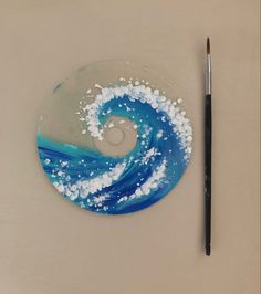 a blue and white painted disc next to a paintbrush on a table with a gray background