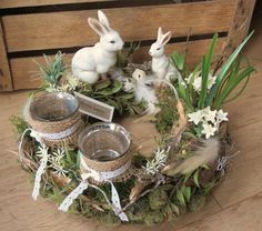 two white rabbits sitting in the middle of a wreath with silver dishes and cups on it