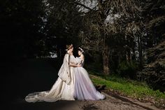 two women in wedding dresses are standing on the side of a road near some trees