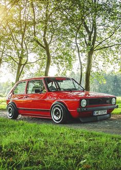 an old red car parked on the side of a road in front of some trees