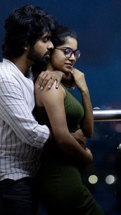 a man and woman standing next to each other in front of a window at night