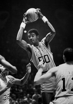 an old black and white photo of a basketball player trying to block the ball from being blocked by two other players