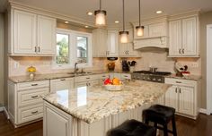 a large kitchen with white cabinets and marble counter tops, two stools in front of the island