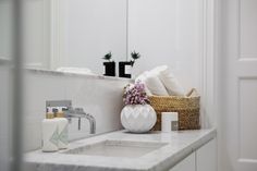 a white bathroom sink sitting under a mirror next to a basket with flowers in it