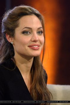 a woman with long brown hair and blue eyes is smiling at the camera while wearing a black top