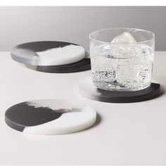 two black and white coasters sitting on top of a table next to a glass