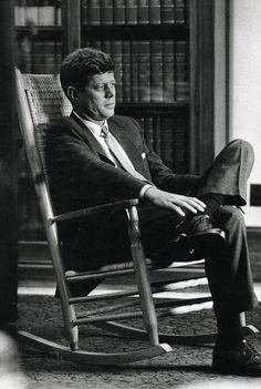 a man sitting in a rocking chair next to a book shelf