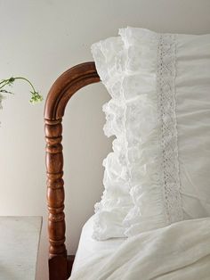 a bed with white ruffled pillows and a wooden headboard next to a plant